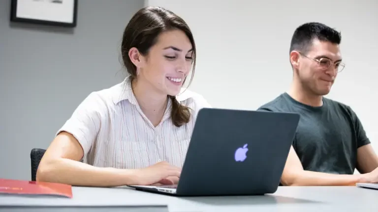 Two students inside classroom on their laptops.